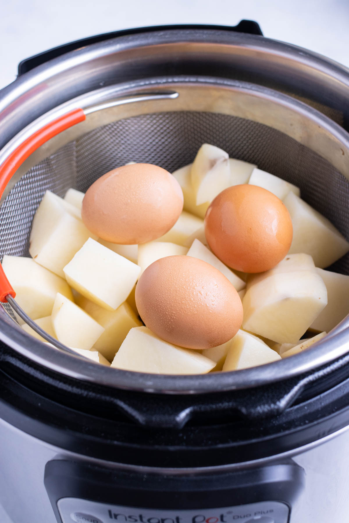 Diced potatoes and eggs are placed inside the instant pot in a vegetable basket.