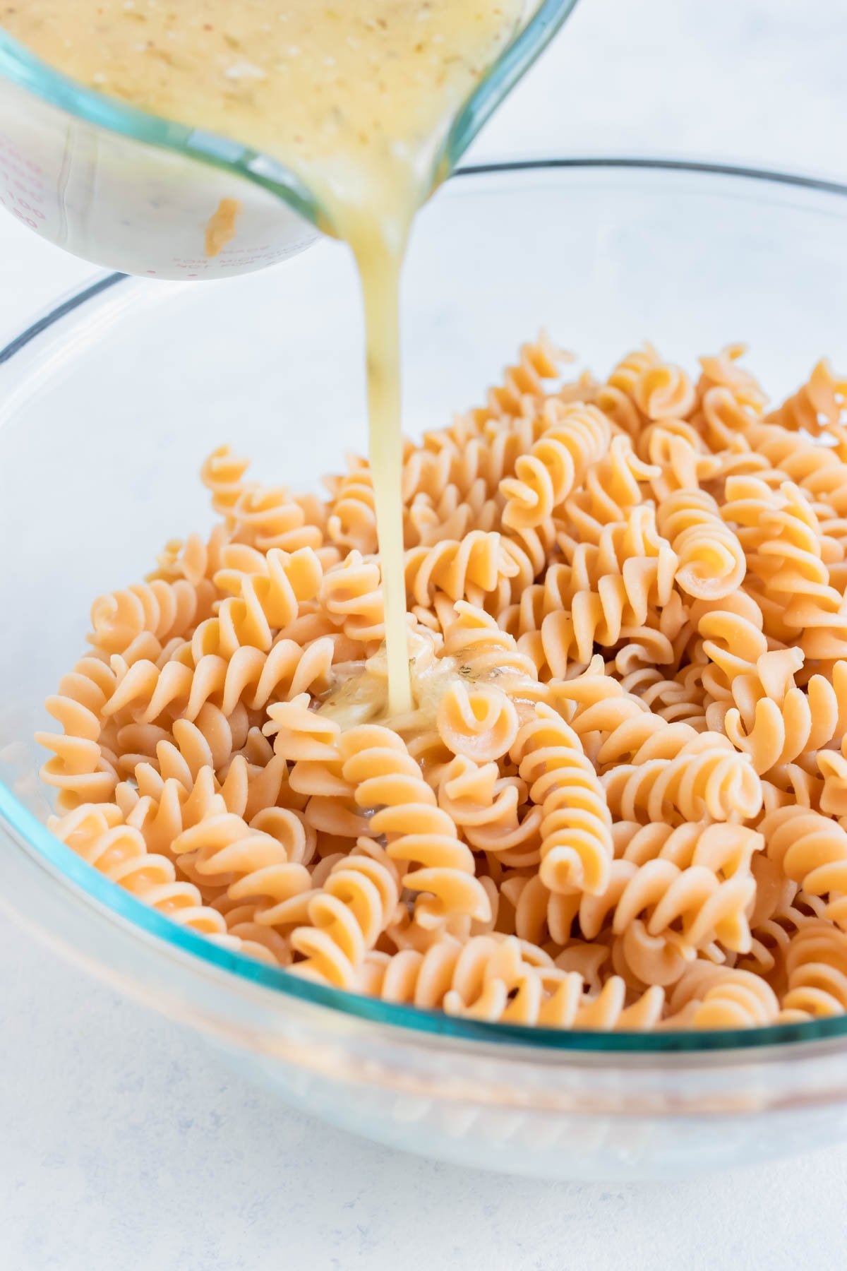 Italian dressing is pour onto the cooked noodles in a bowl.