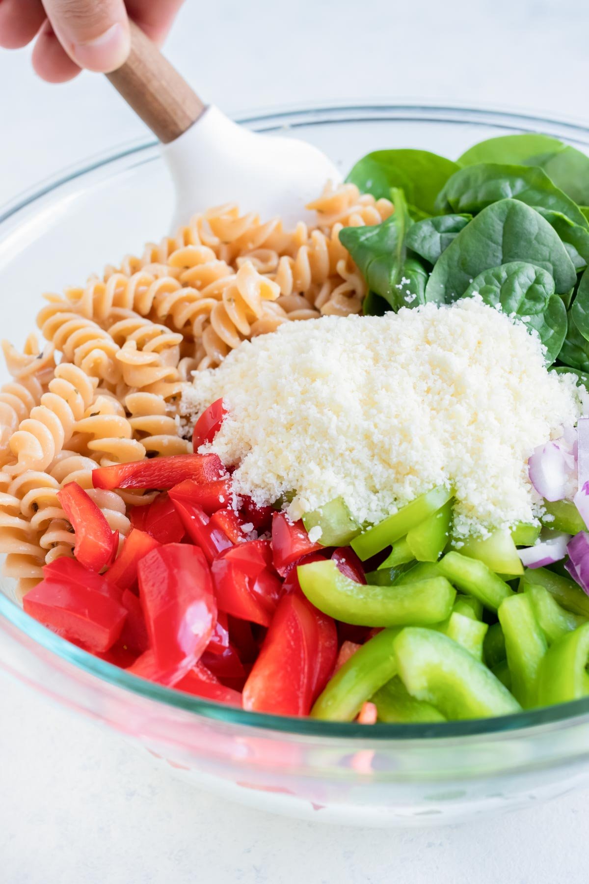 Chopped veggies, spinach, and Parmesan cheese are added to the bowl of noodles.