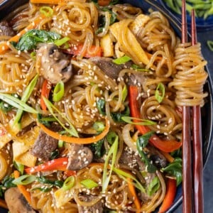 A bowl of a Korean Japchae recipe full of glass noodles, veggies, and marinate beef is being eaten with chopsticks.