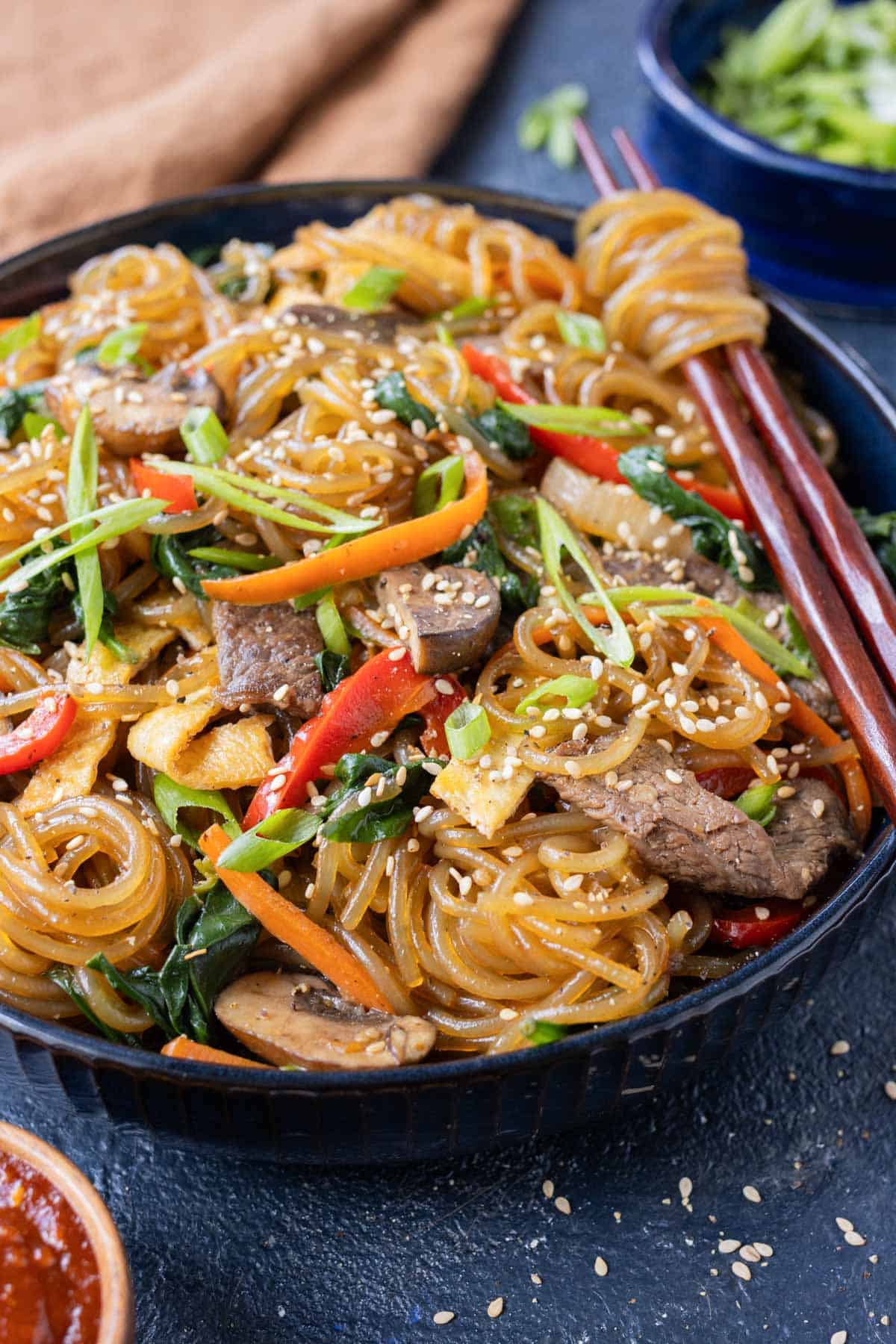Glass noodles in a Japchae recipe are twirled by chopsticks.