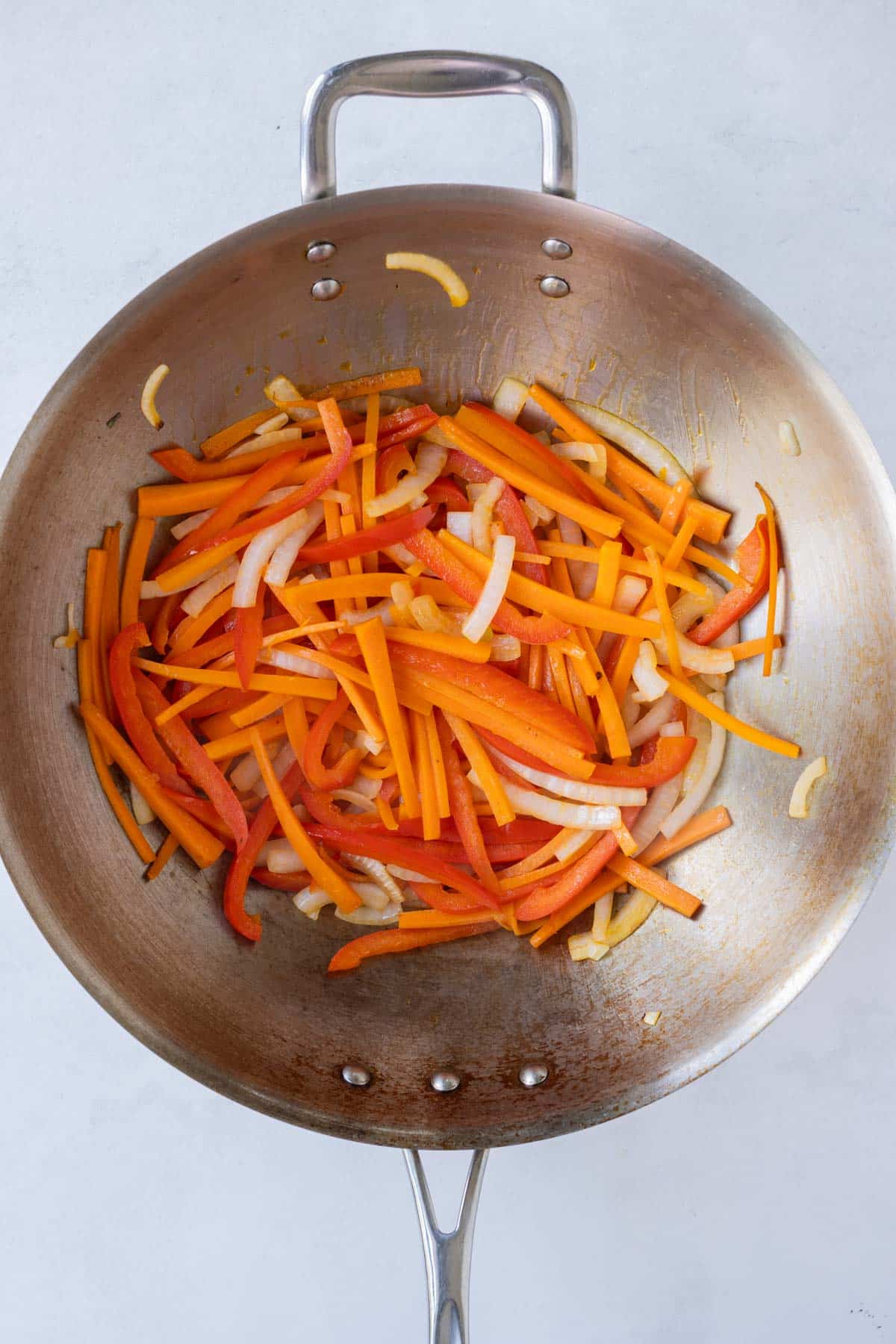 Bell peppers and onions are cooked in a skillet.