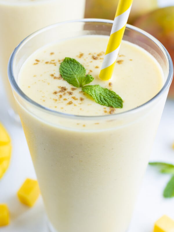 A glass is filled with a smooth and creamy Mango Lassi recipe with a straw.