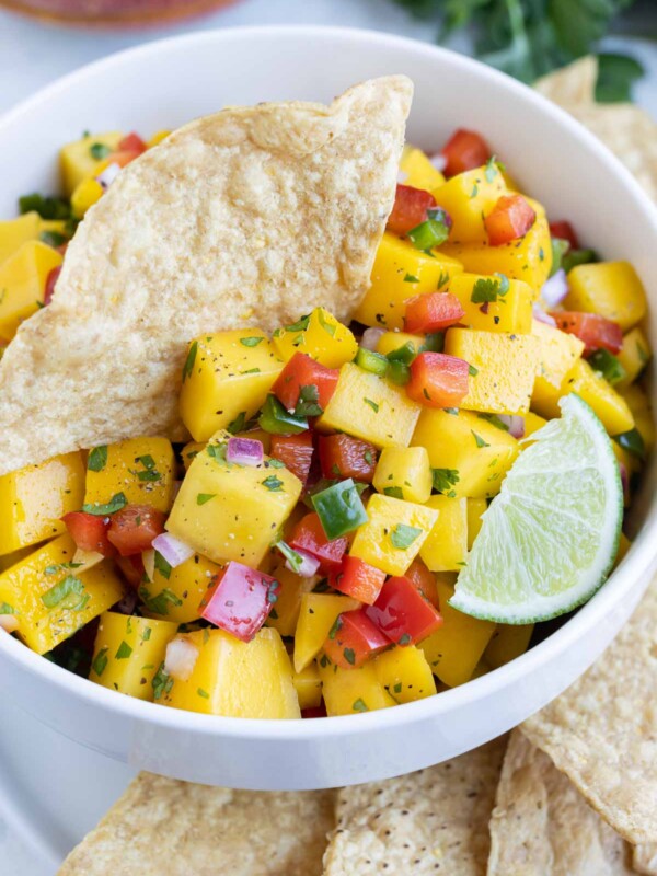 A white bowl is filled with mango salsa and served with tortilla chips.