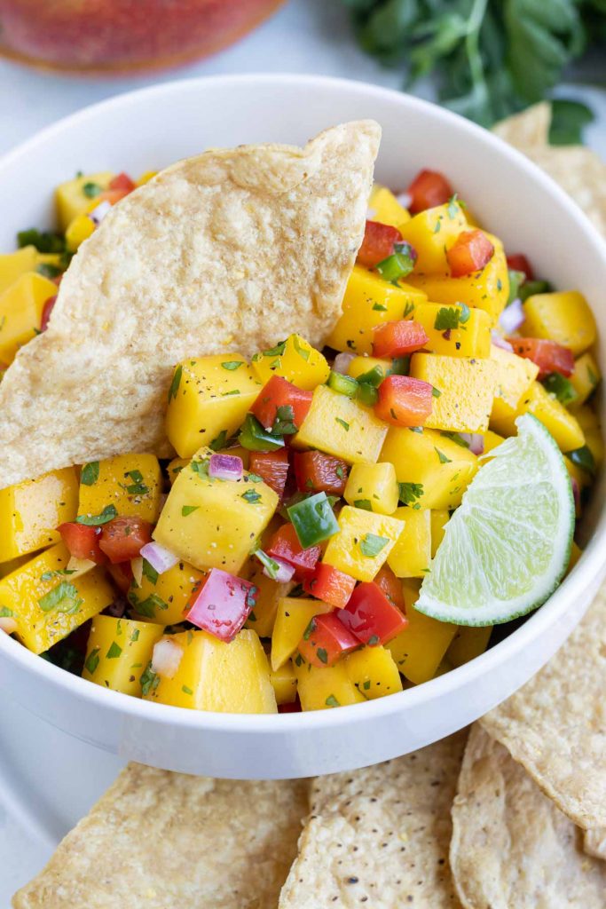 A white bowl is filled with mango salsa and served with tortilla chips.