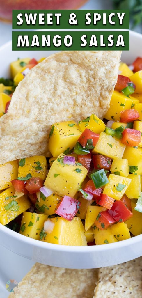 A white bowl is filled with mango salsa and served with tortilla chips.