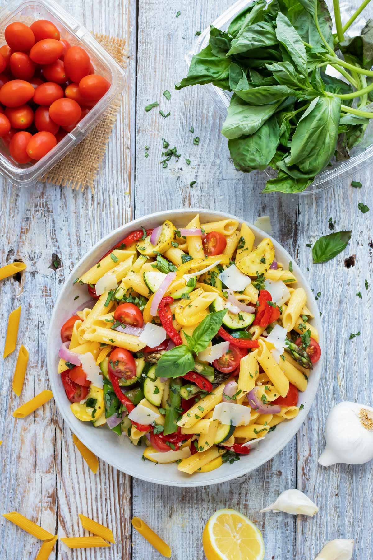 A pint of tomatoes, fresh basil, and a bowl full of pasta primavera.