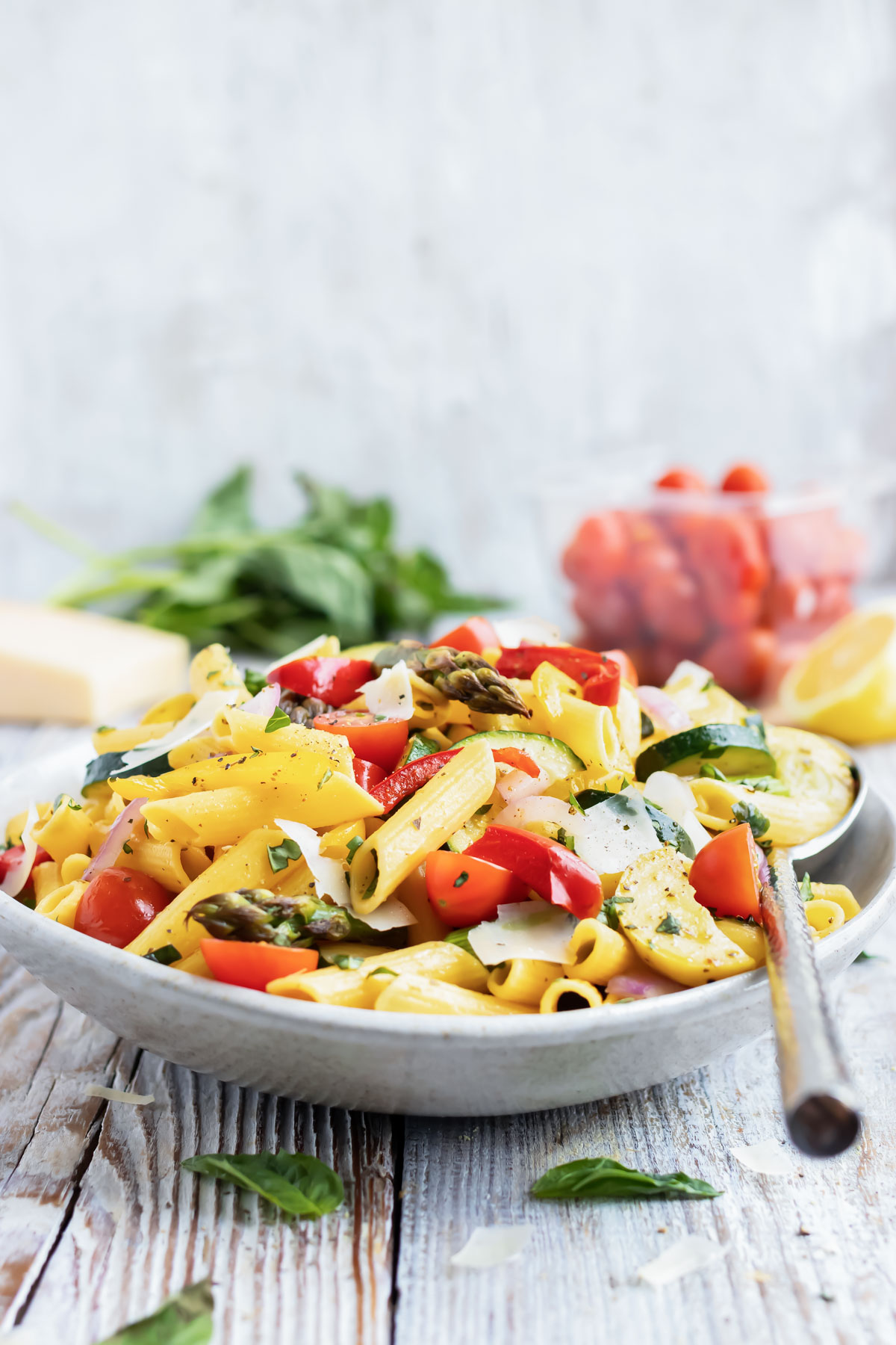 A serving bowl full of a pasta primavera recipe with a silver spoon.
