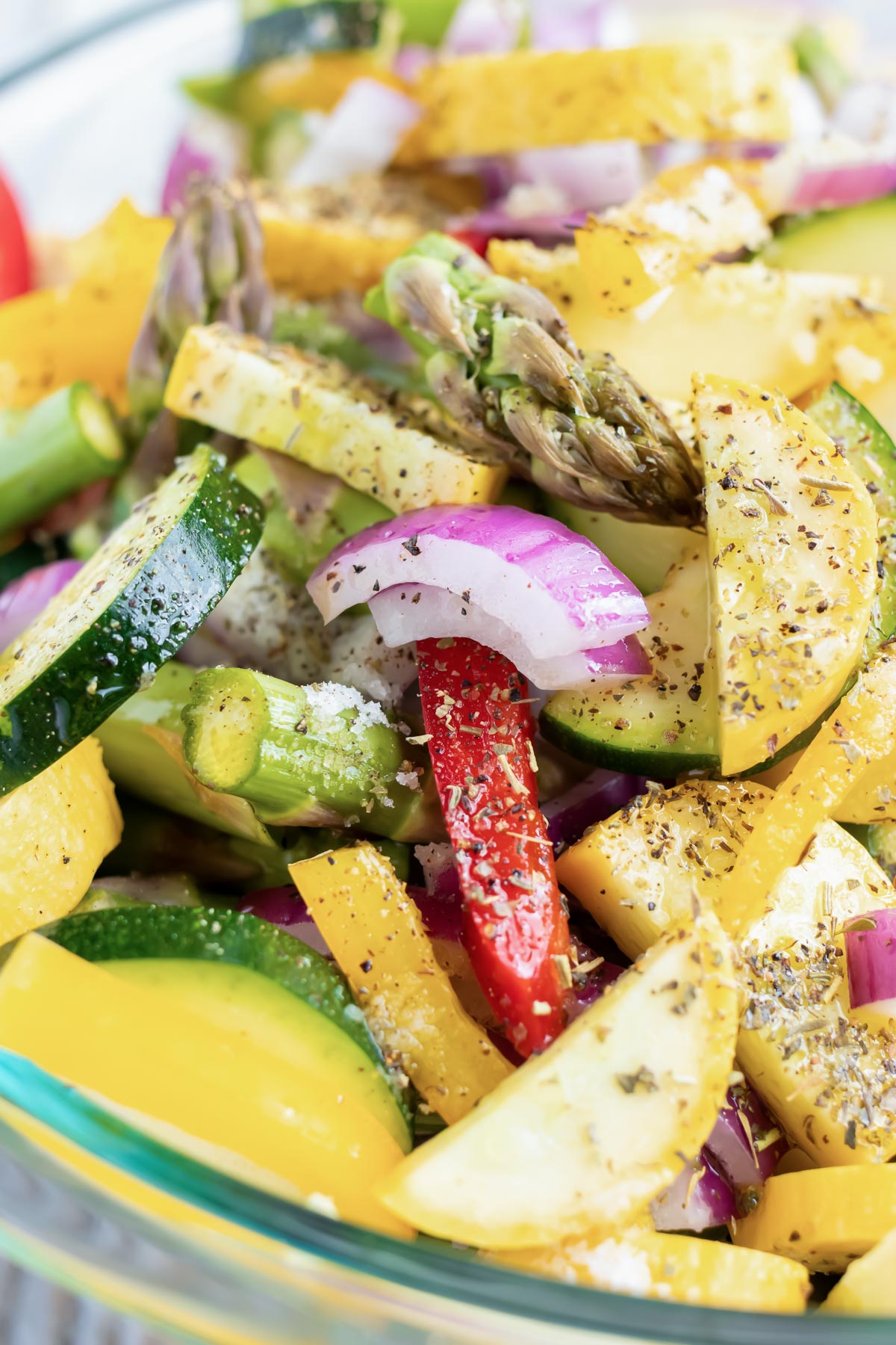 Chopped veggies with oil and seasonings in a glass bowl.