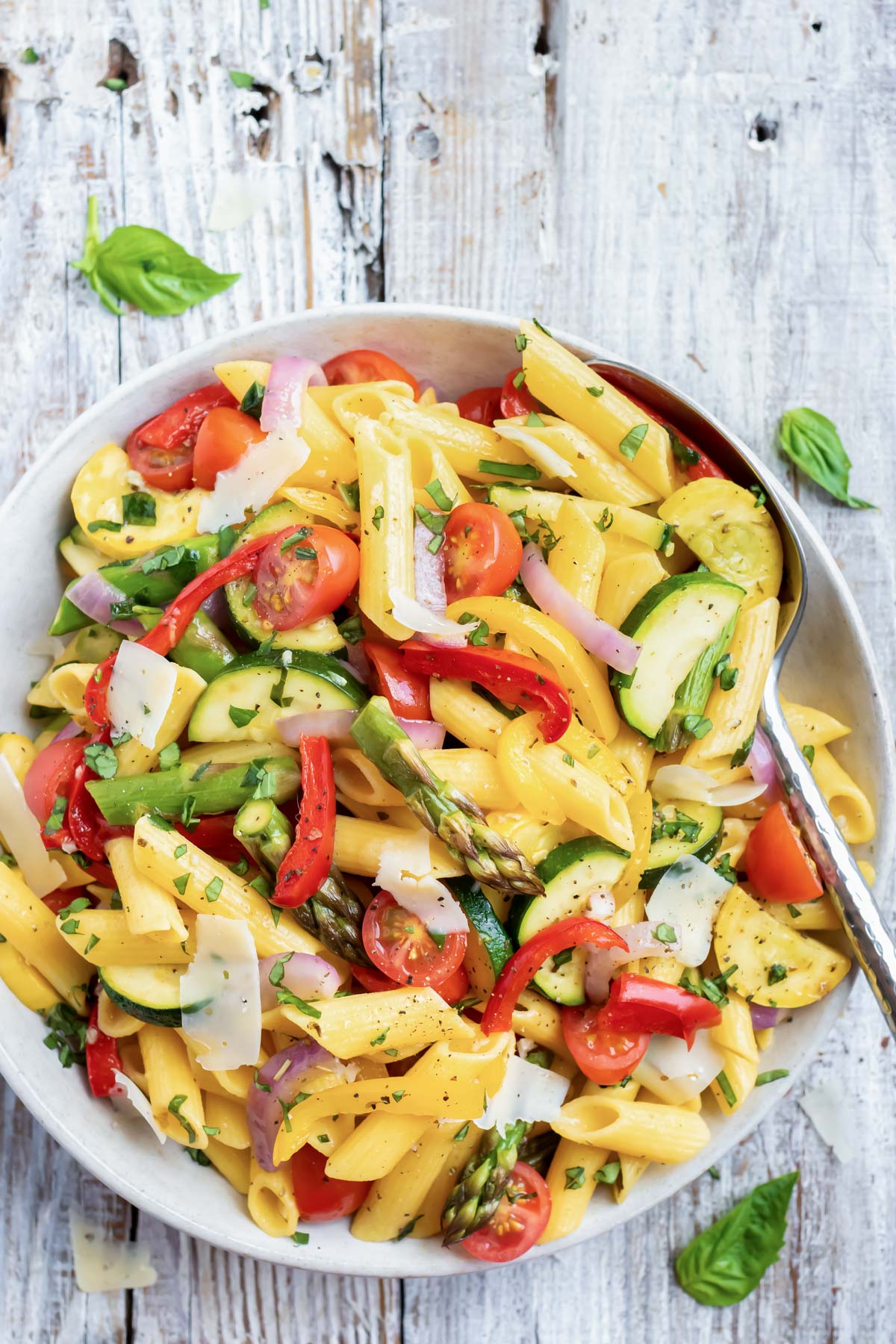 A large white bowl full of an easy and healthy roasted vegetable pasta with tomatoes, asparagus, and bell peppers.