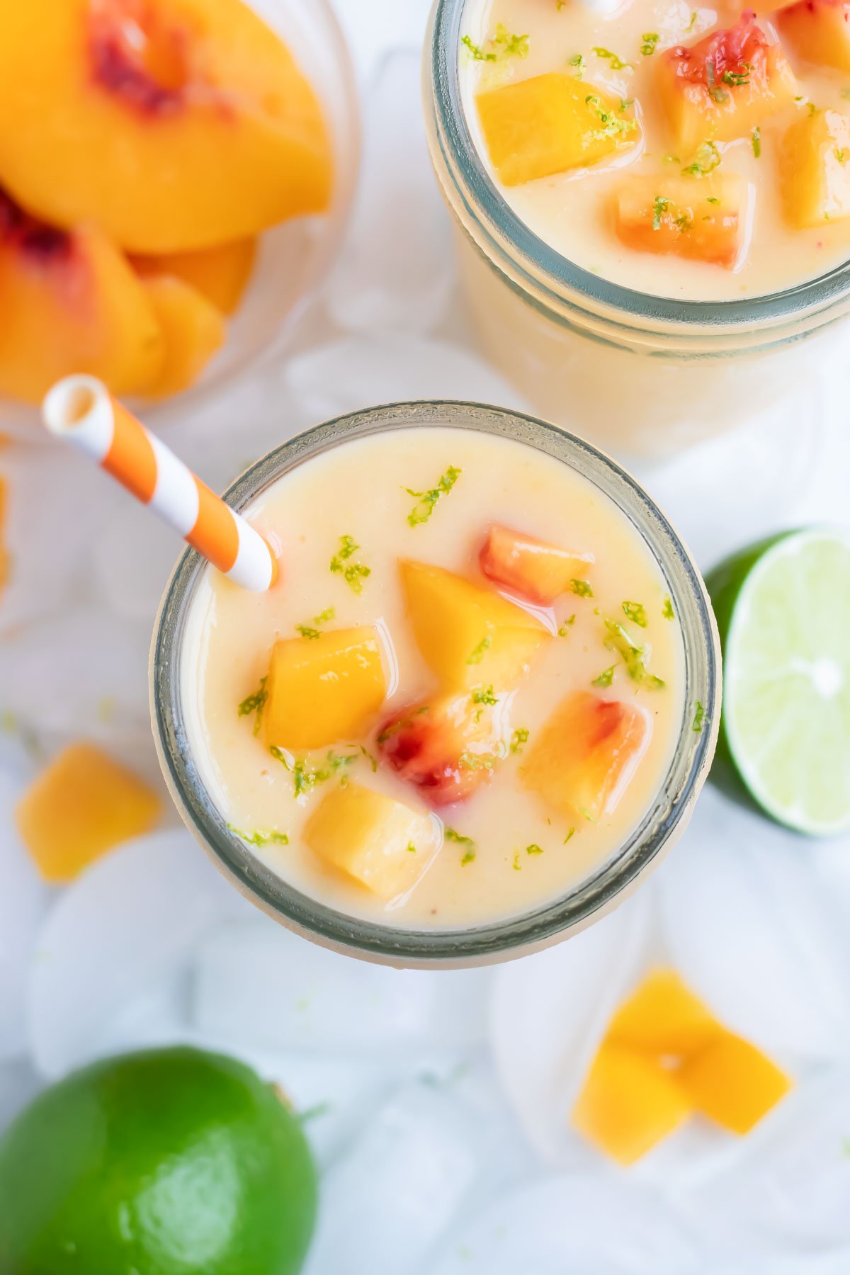 A peach smoothie is topped with peaches and lime zest for a frozen drink.