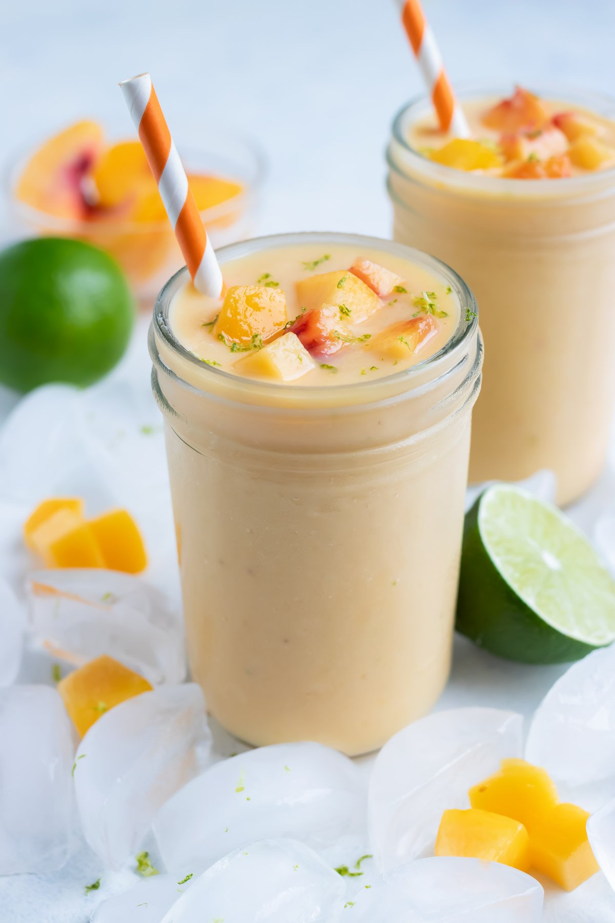 Two glasses are used to hold a thick and creamy peach smoothie.