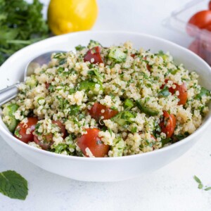 Light Quinoa Tabbouleh is served from a white bowl near fresh herbs and tomatoes.