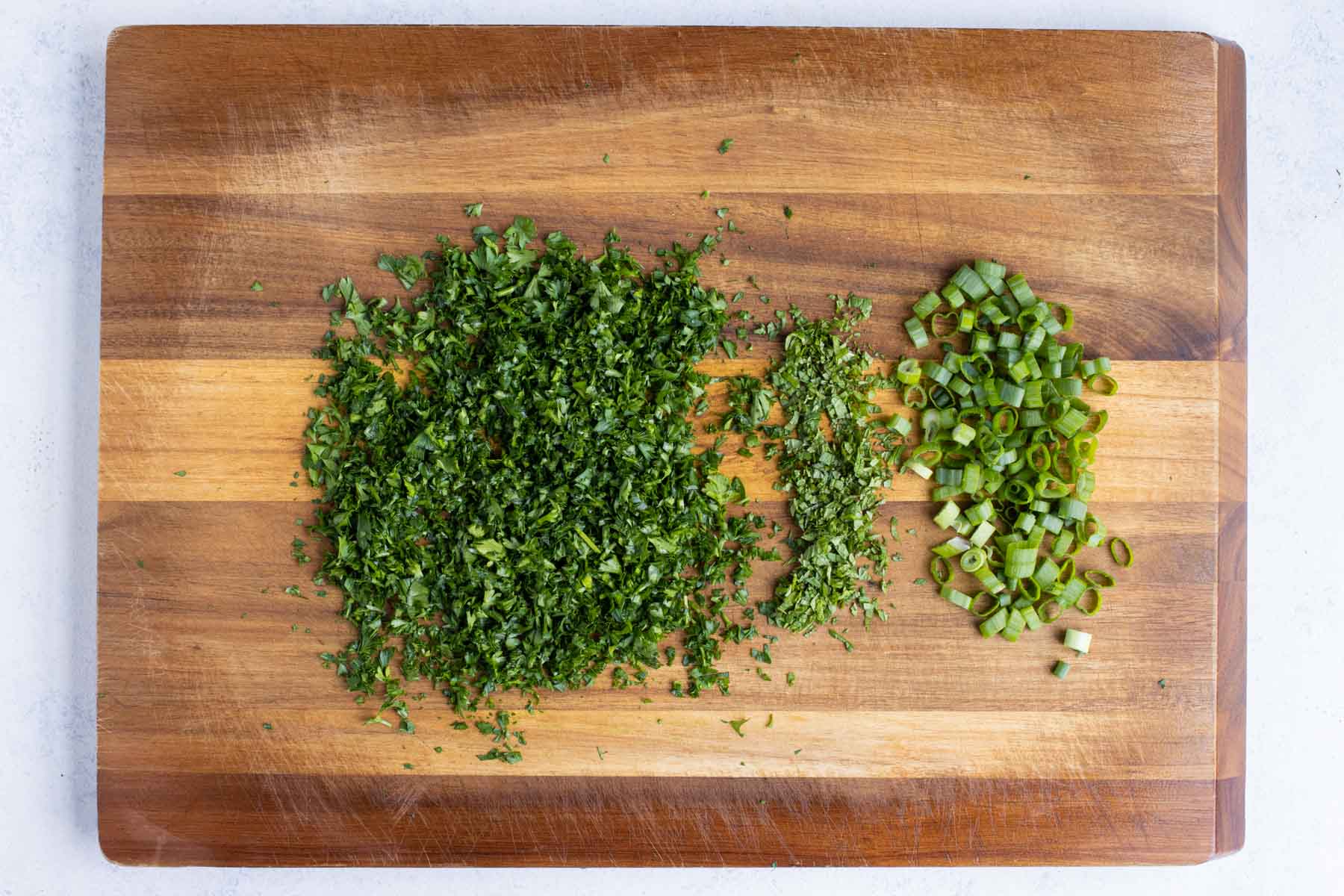 Parsley, green onions, and fresh mint are chopped on a cutting board.