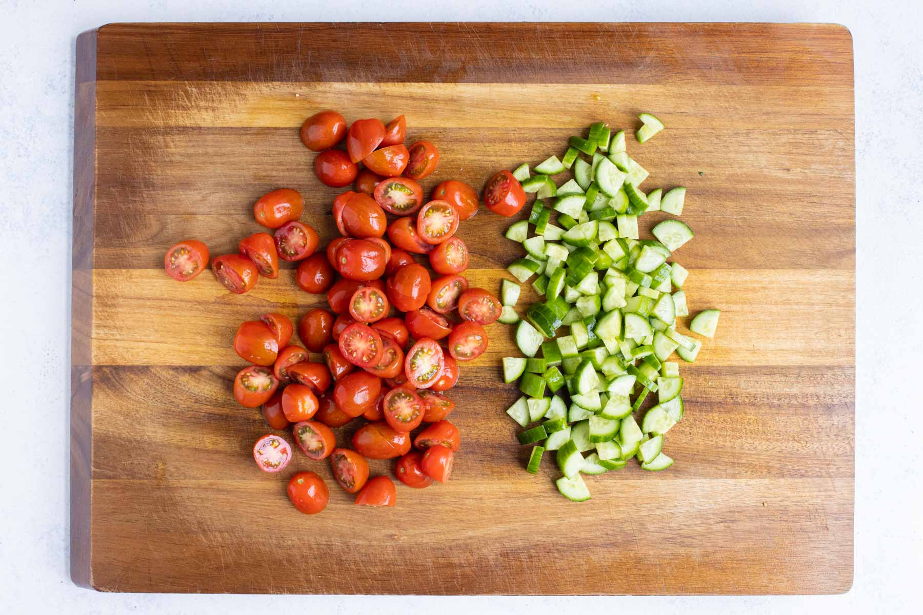 Cherry tomatoes and cucumbers are chopped on a cutting board.