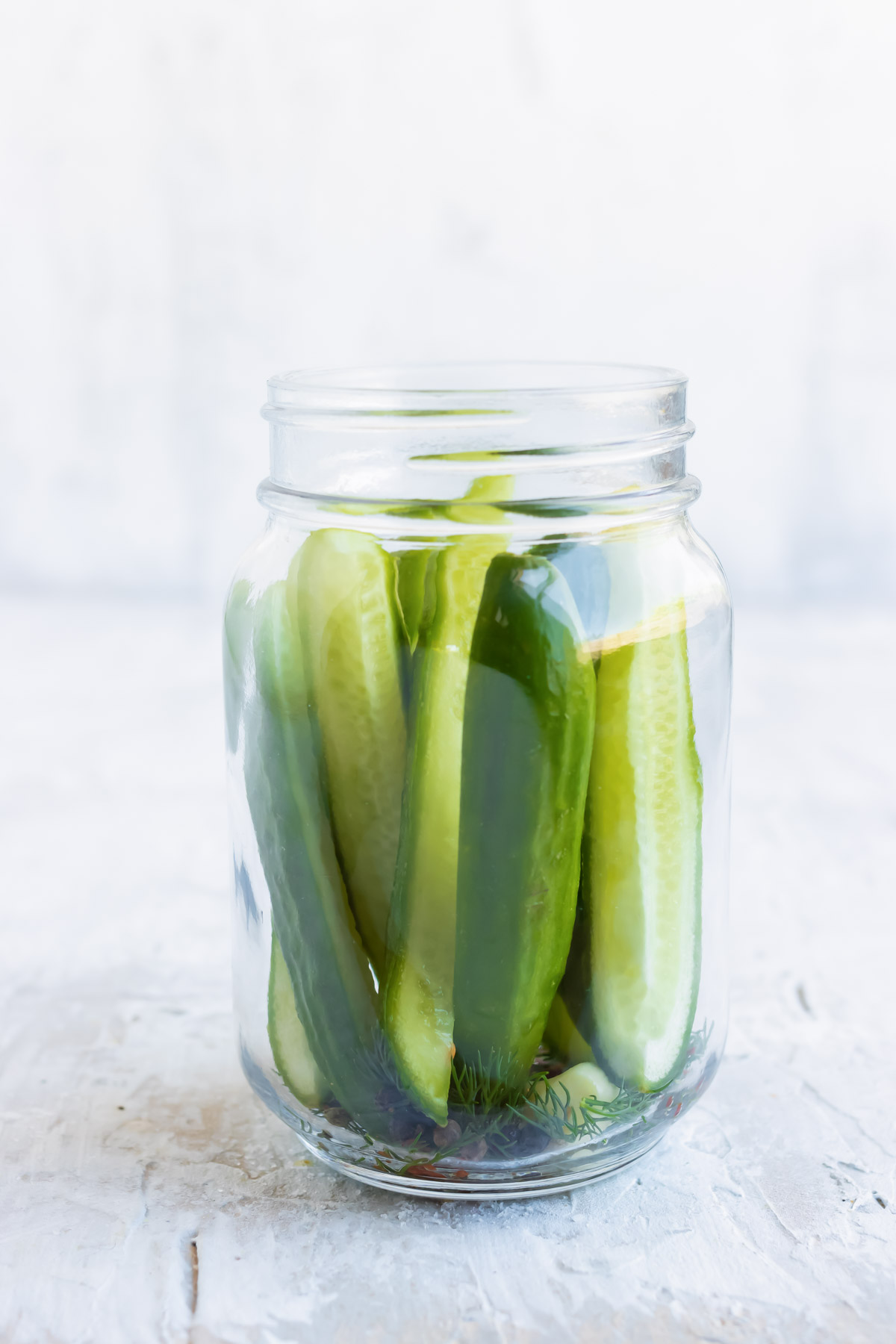 Sliced cucumbers are added to a jar with spices.