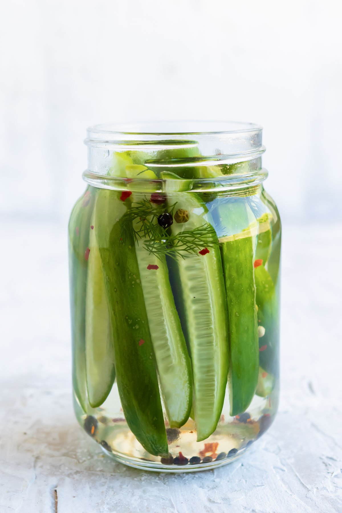 A mason jar is full with cucumbers, spices, and brine.