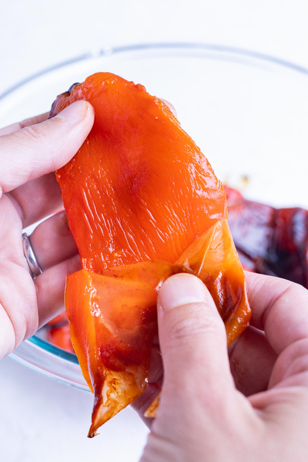 A hand gently pulls the skin off roasted peppers.