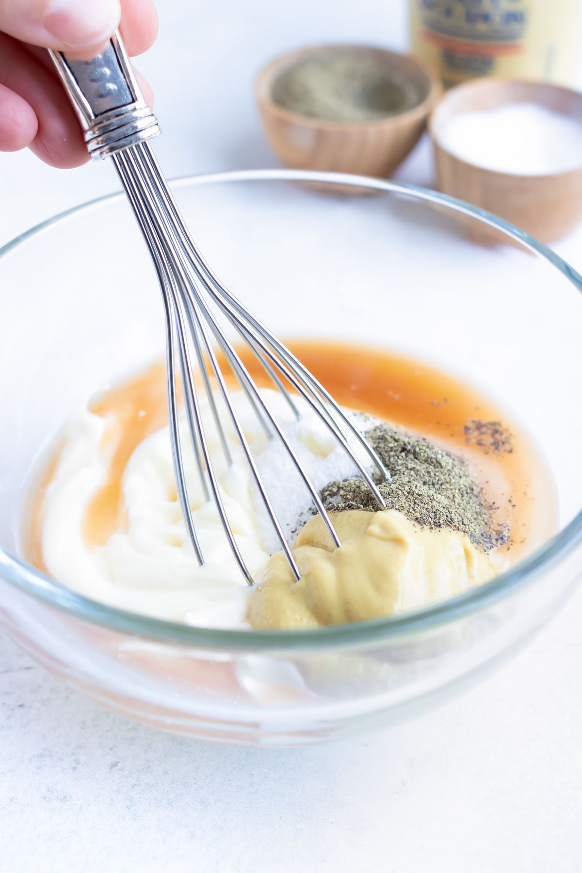 Creamy coleslaw dressing ingredients in a clear, glass bowl.