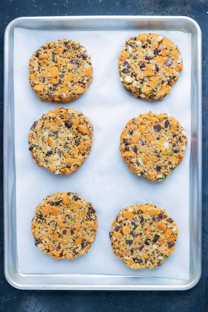 Six formed meatless sweet potato quinoa burger patties on a parchment-lined sheet pan.