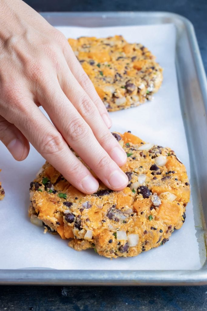 Hands pressing the mixture into a one-inch thick sweet potato black bean burger patty on parchment paper.