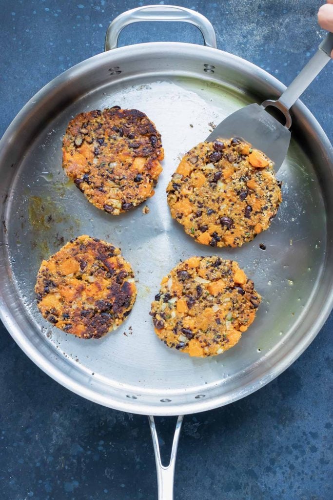 Sweet potato black bean burger patties cooking in a single layer in a stainless steel skillet.