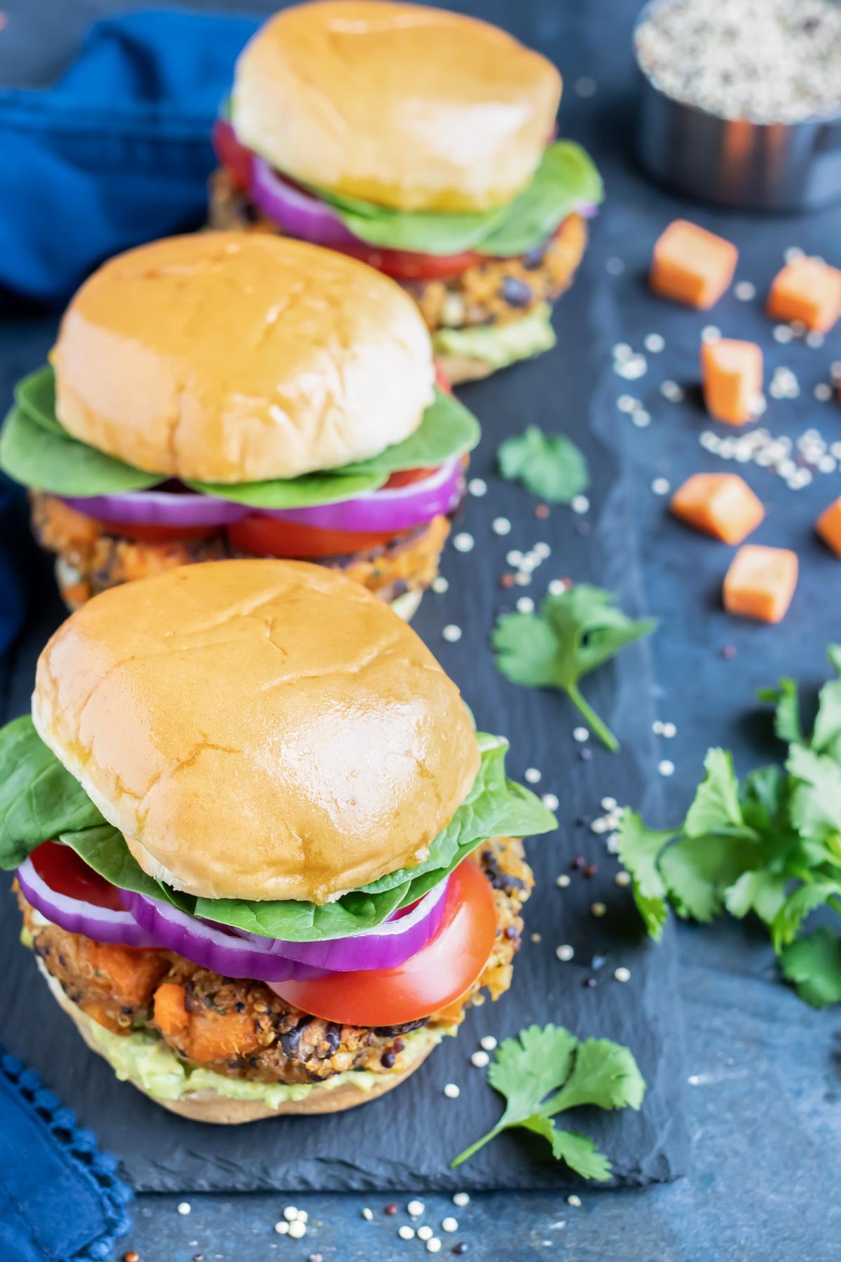 Three veggie burgers in a row with sweet potatoes, quinoa, and black beans.