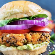 Sweet potato black bean veggie burger patty on a gluten-free bun with red onion, tomatoes, and lettuce.