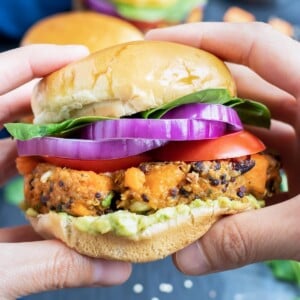 Two hands holding a healthy black bean quinoa burger with sweet potatoes, red onion, and avocado.