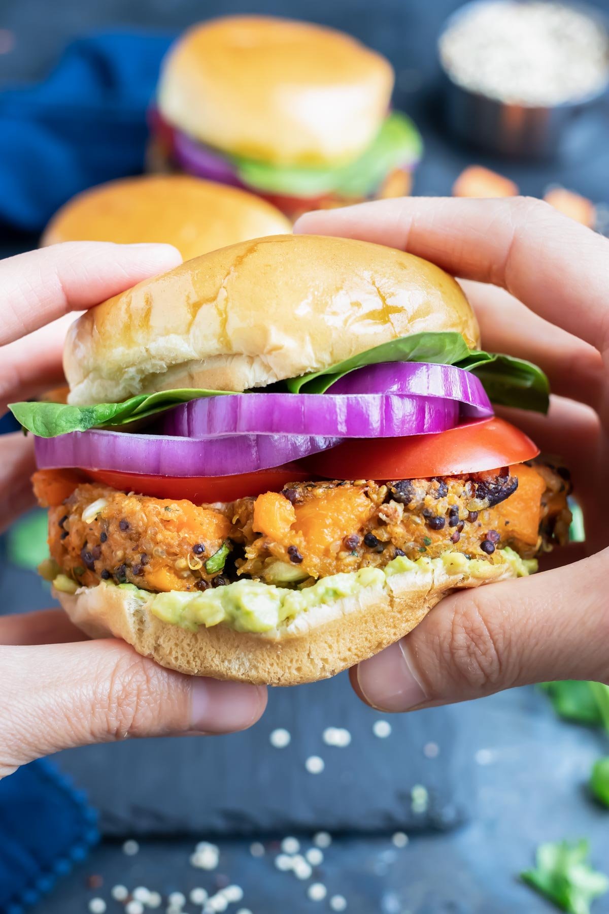 Two hands holding a healthy black bean quinoa burger with sweet potatoes, red onion, and avocado.