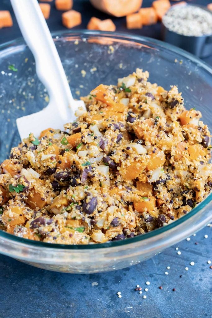 Sweet potatoes, black beans, quinoa, and oat flour being mixed in a glass bowl for vegan burgers.