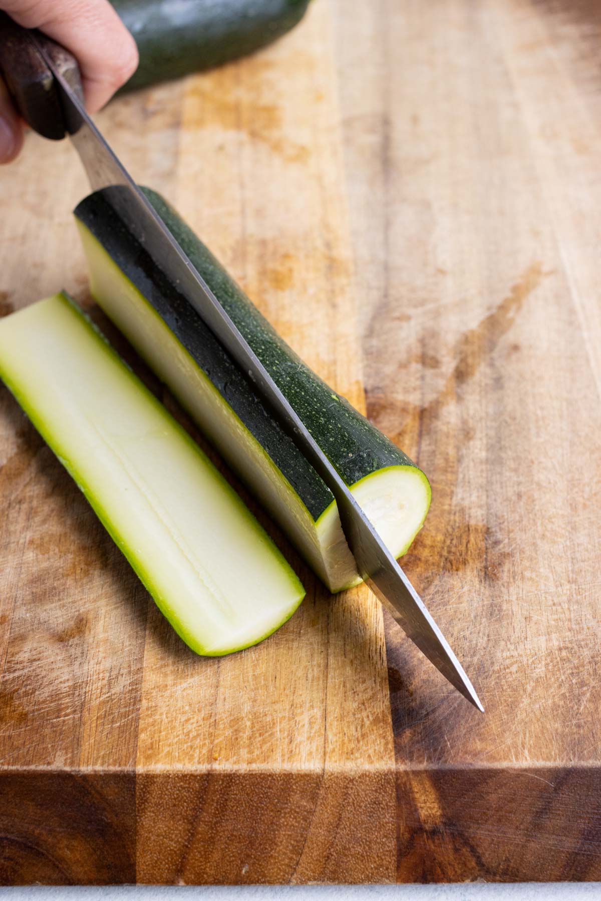 A knife cuts a zucchini into strips for lasagna