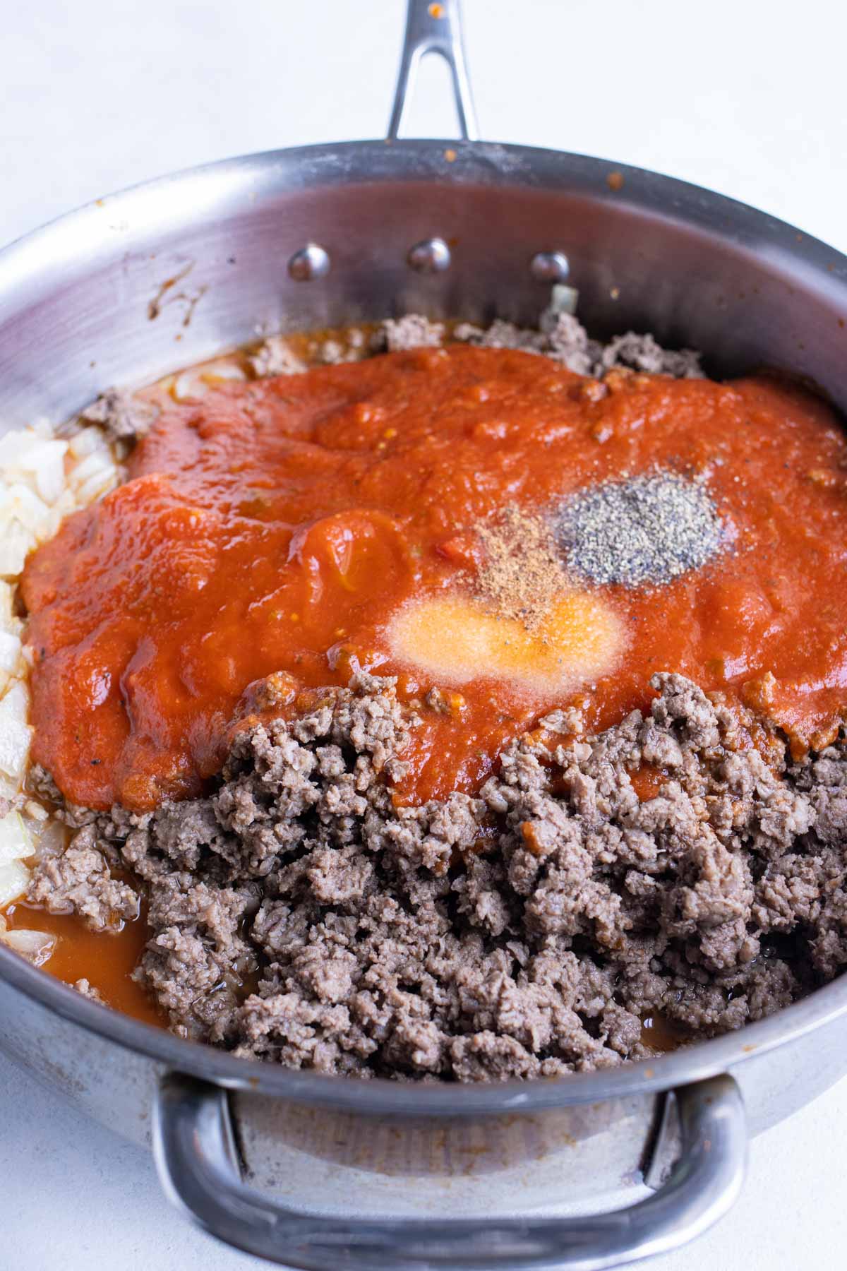 Tomato sauce is added to a skillet of cooked meat.