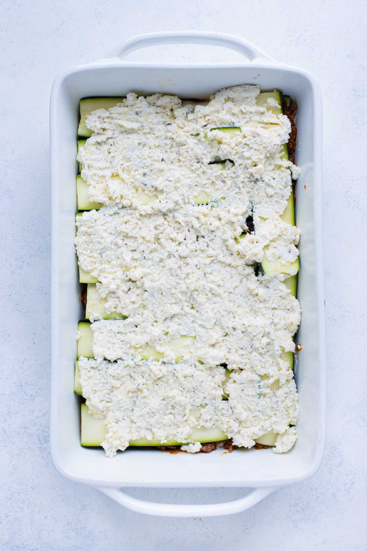 A second layer of ricotta cheese mixture is spread on top of the zucchini strips.