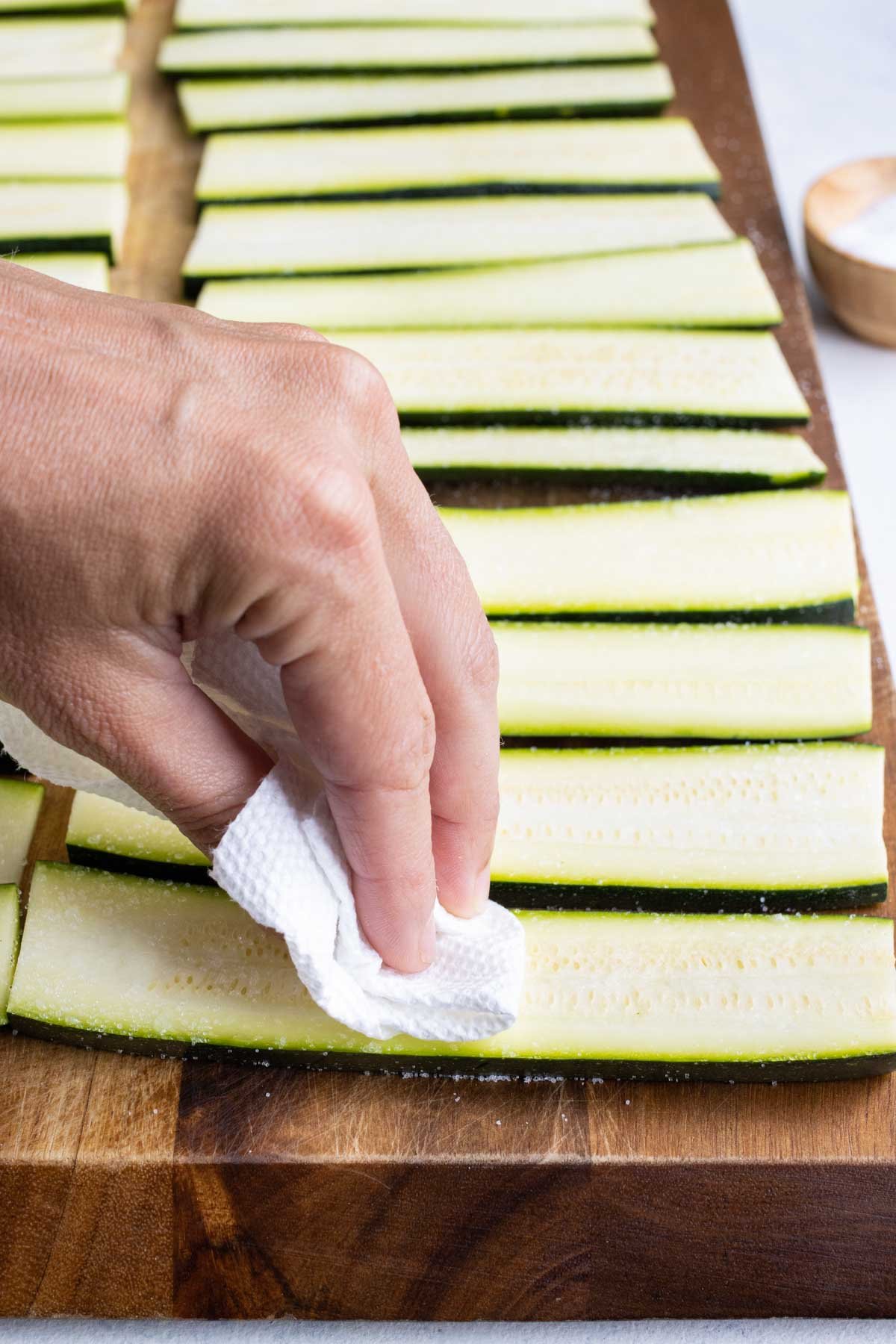 A paper towel wipes excess moisture off a zucchini strip.