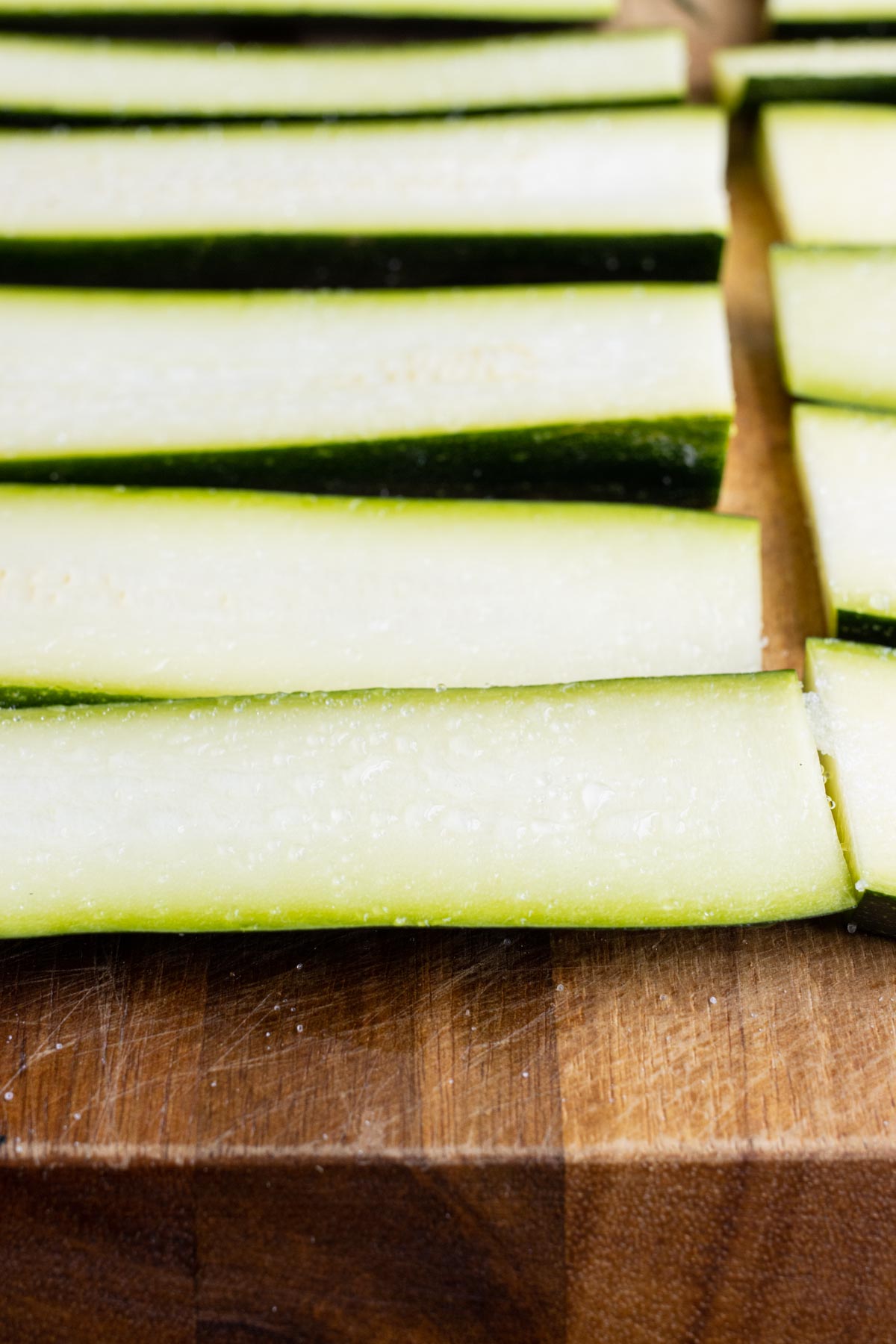 Strips of zucchini are laid out on a cutting board.