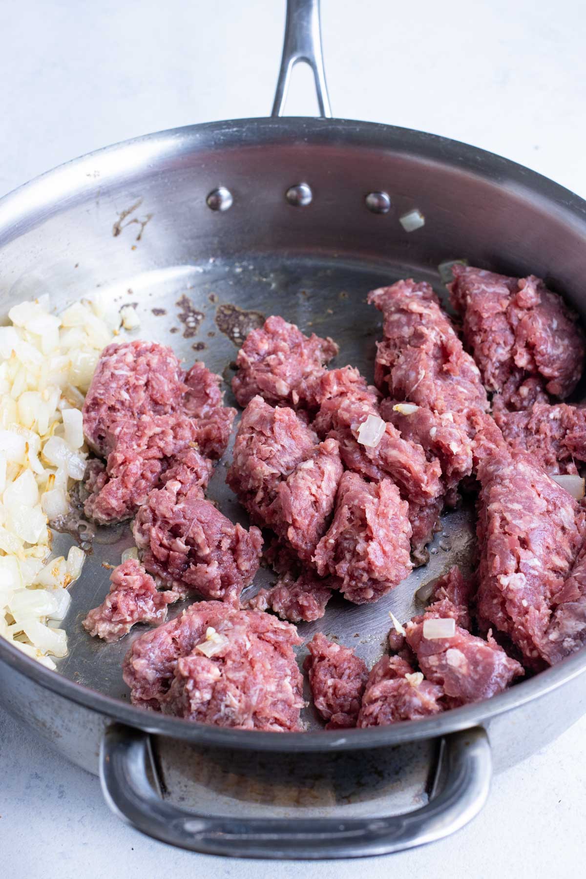 Ground meat is added to a skillet with onions and garlic.