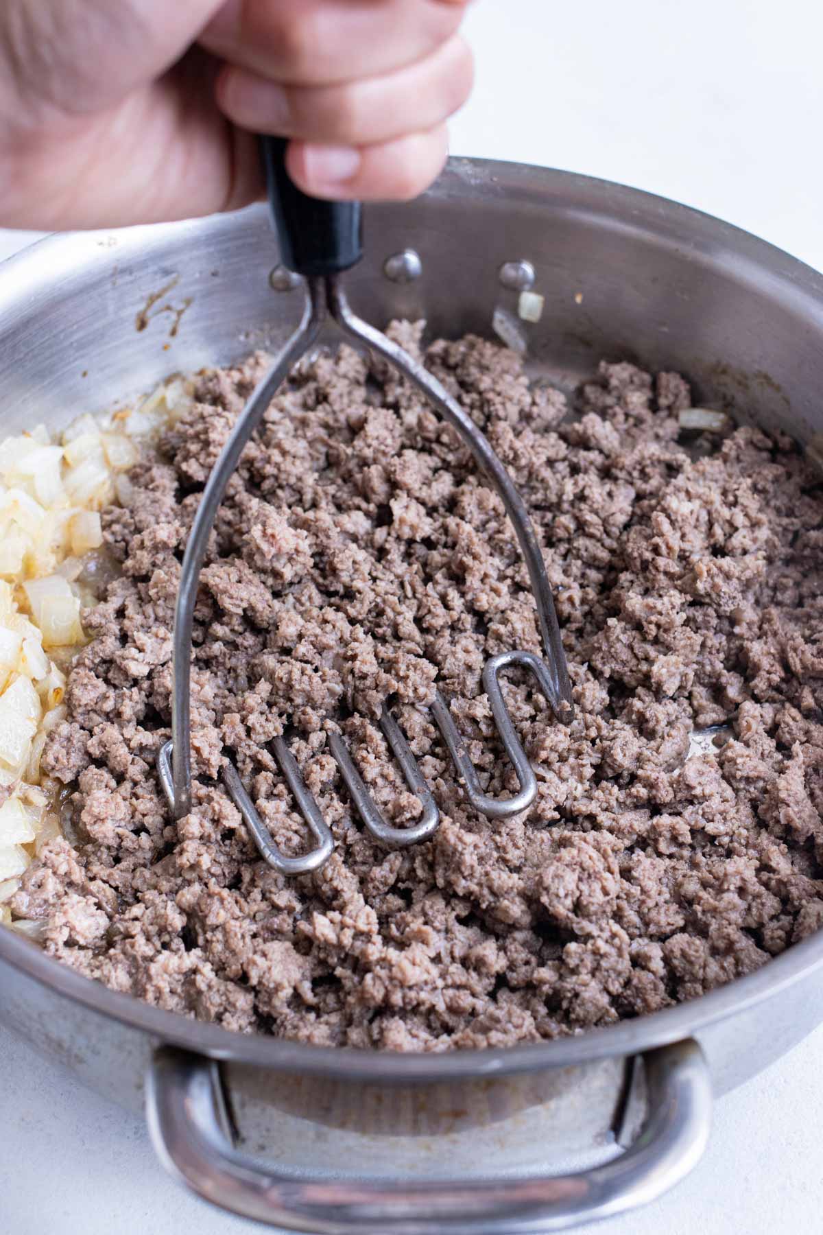 A potato masher breaks up cooked ground meat.