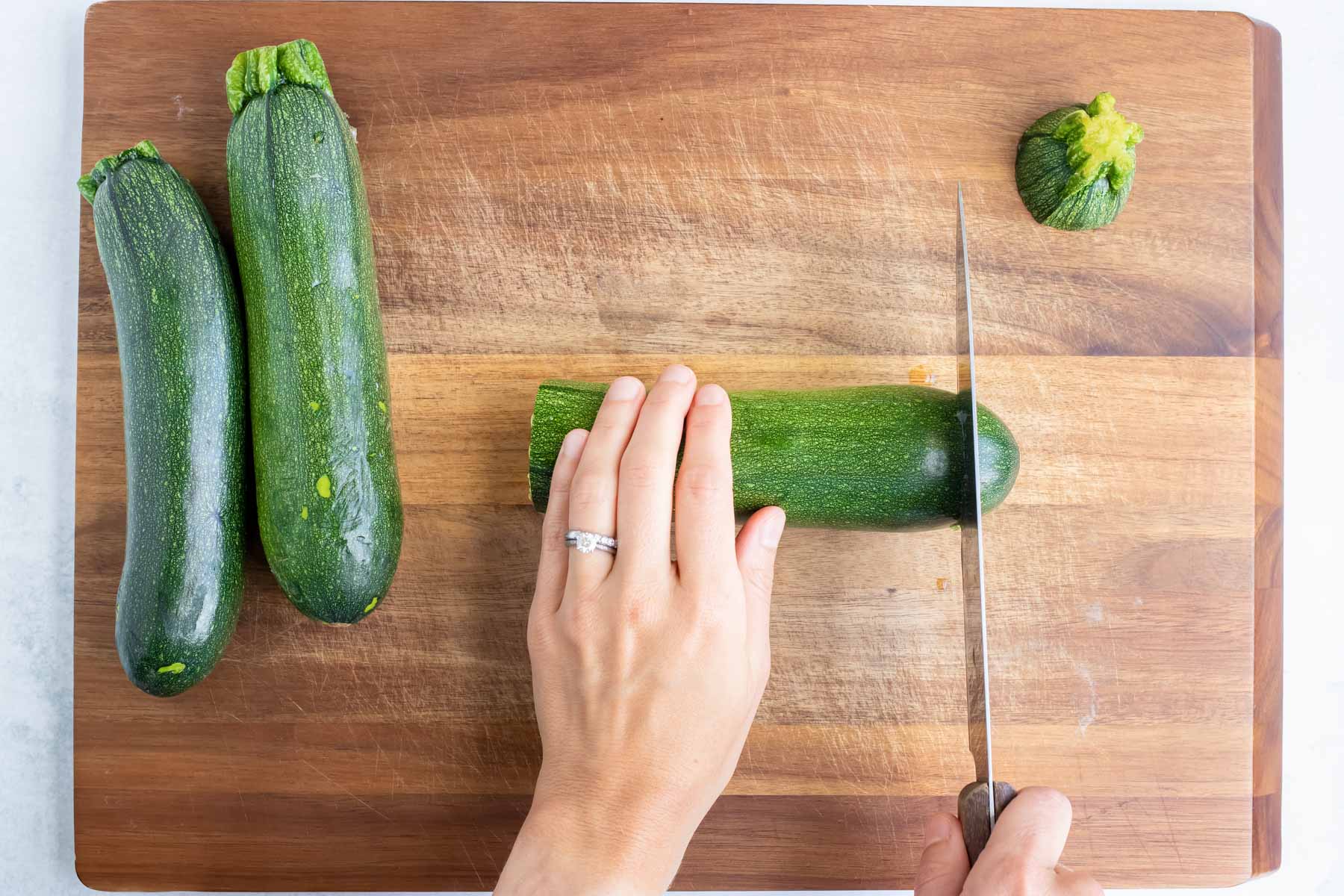 A sharp knife slices off the end of a zucchini on a wooden cutting board.