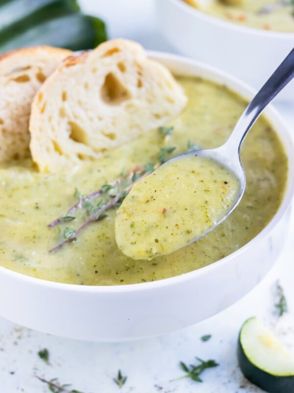 A metal spoon lifts homemade zucchini soup from a bowl.