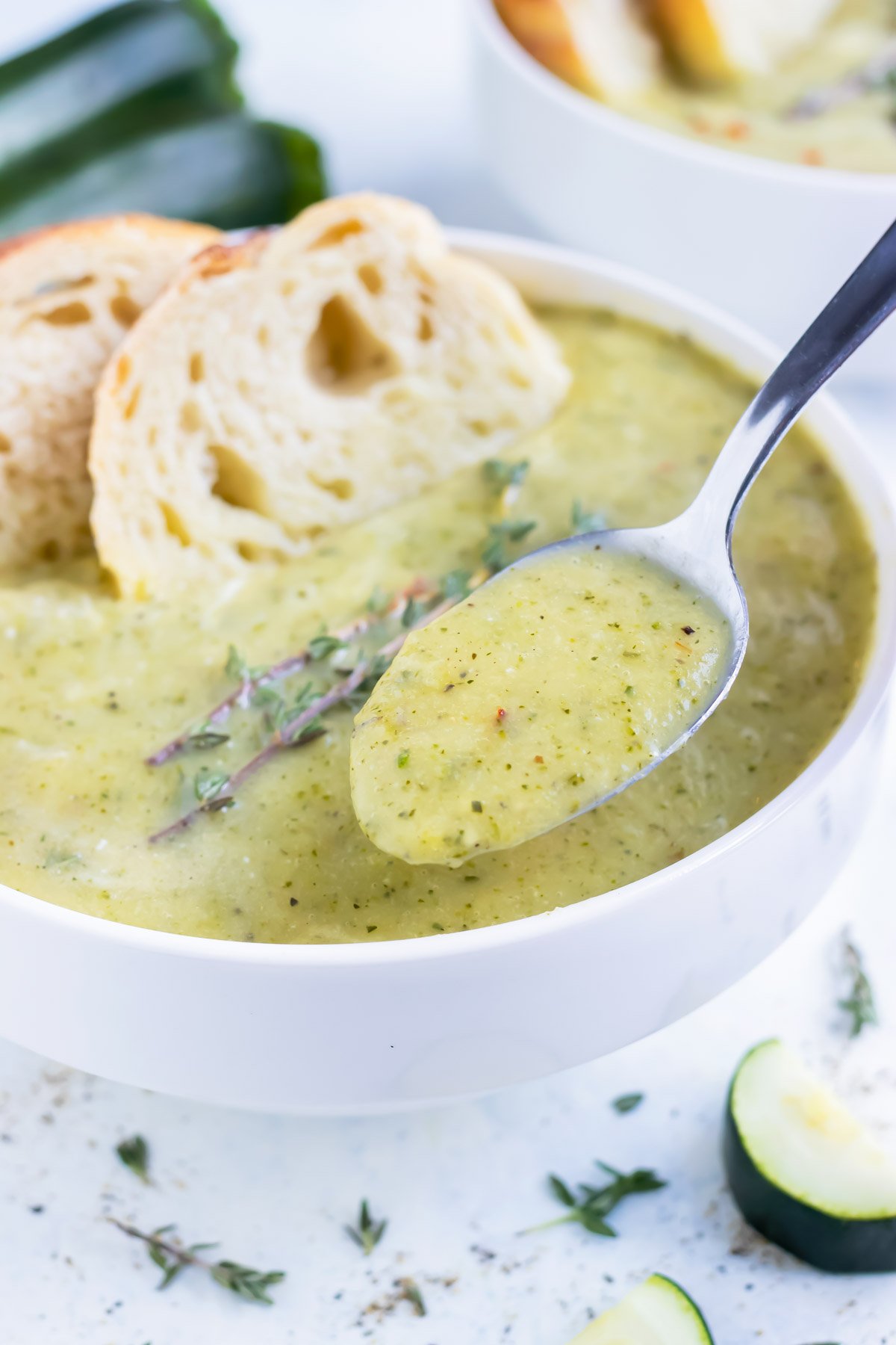 A metal spoon lifts homemade zucchini soup from a bowl.