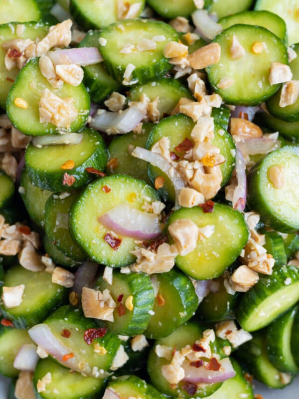 A close up shot of cucumbers with onions, cashews, and dressing.