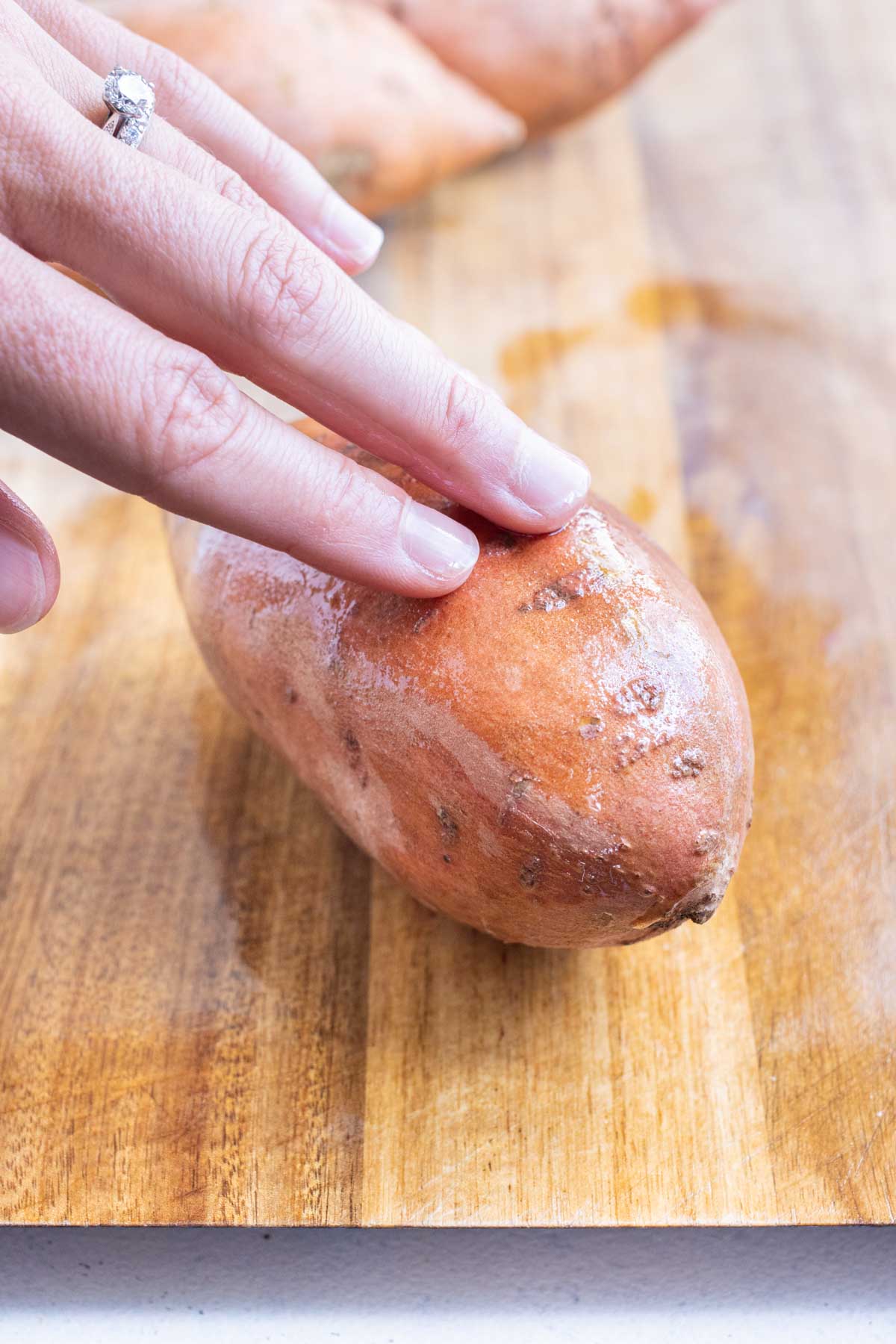 Fingers rub the oil into the skin of a sweet potato.