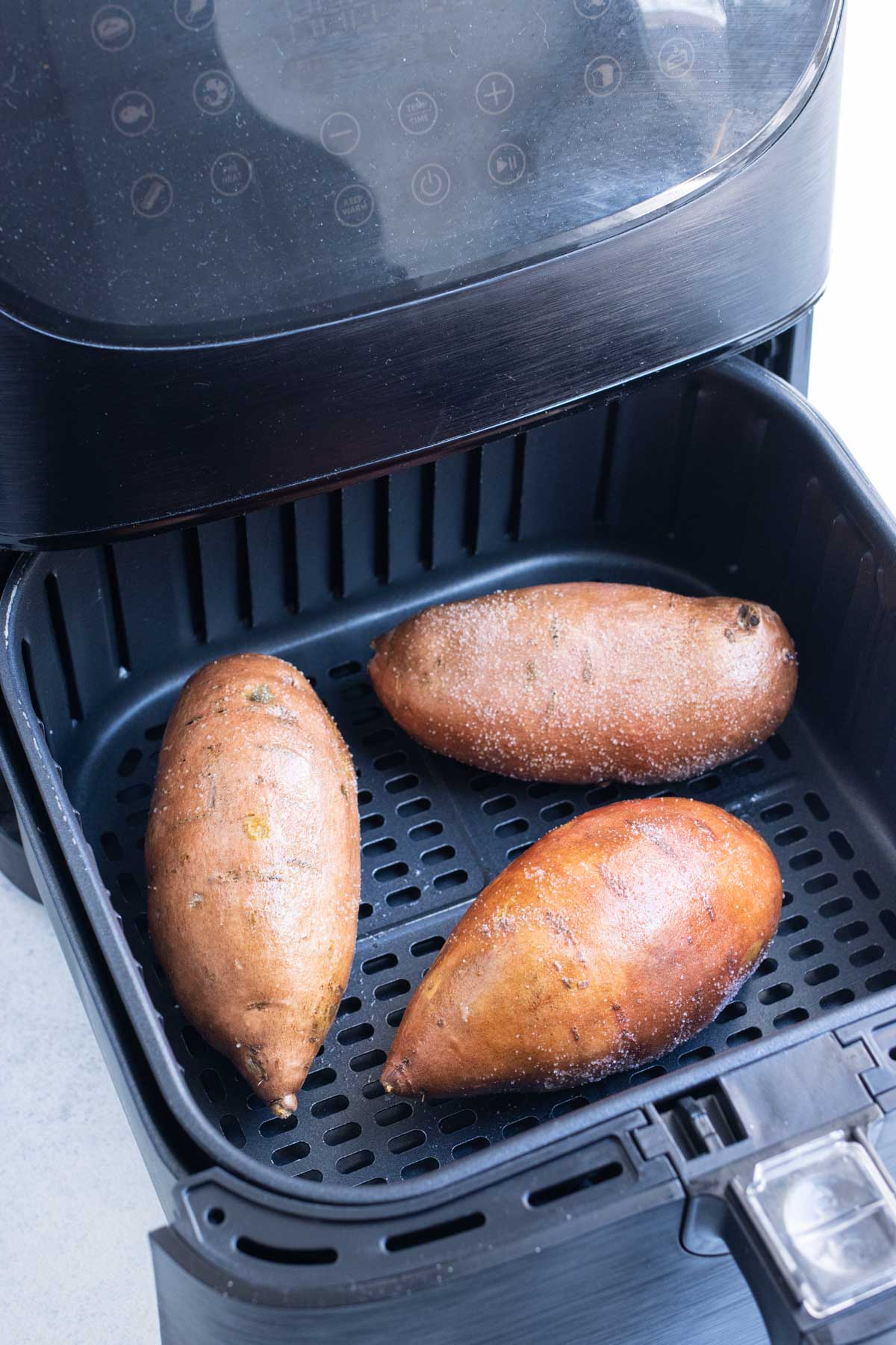 Three sweet potatoes are lined in an air fryer.