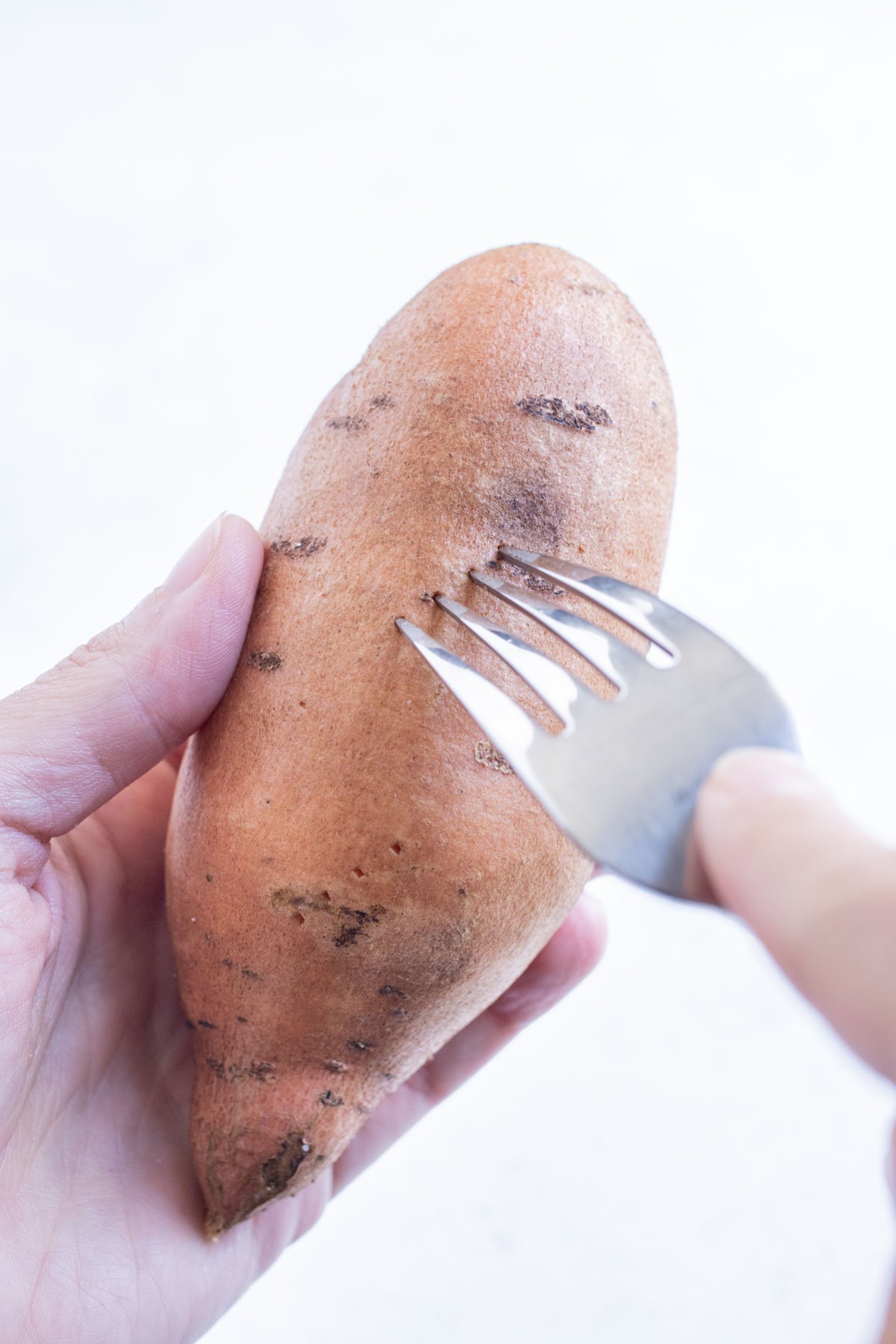A fork pokes the skin of the sweet potato.
