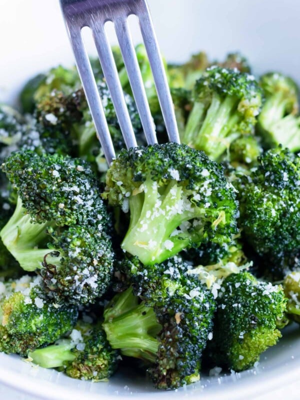 A fork is picking up a floret of air fryer roasted broccoli from a bowl.