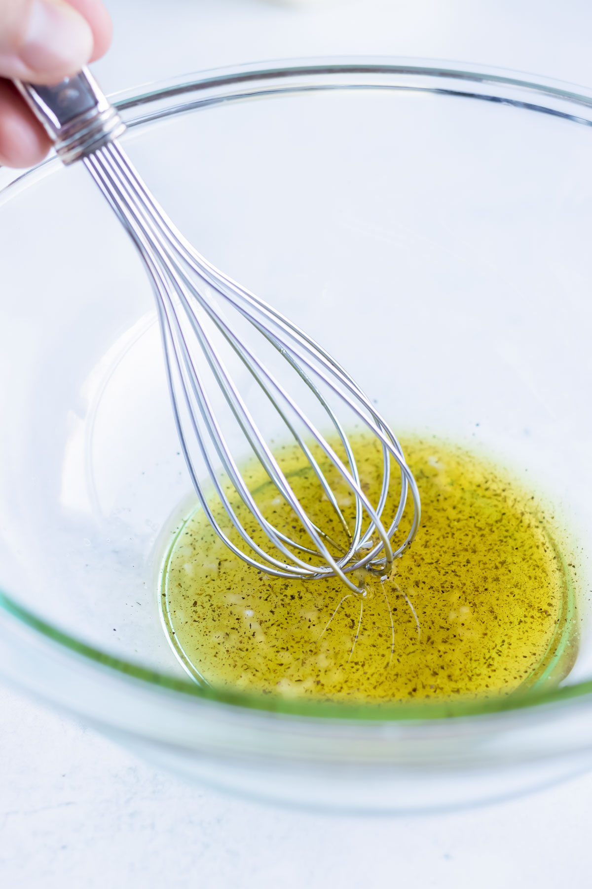 Oil, garlic, salt, and pepper are whisked together in a bowl.