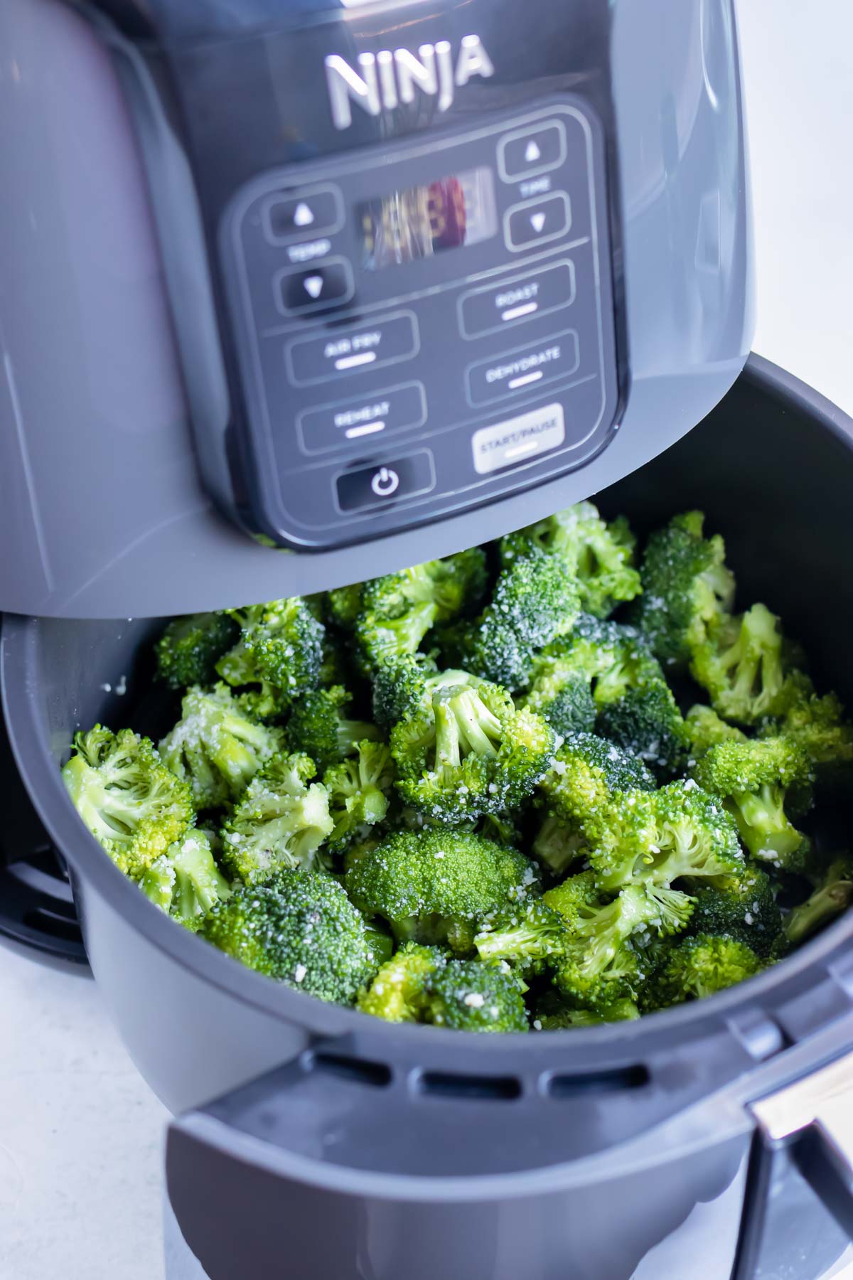 Broccoli florets are in an air fryer basket before cooking.
