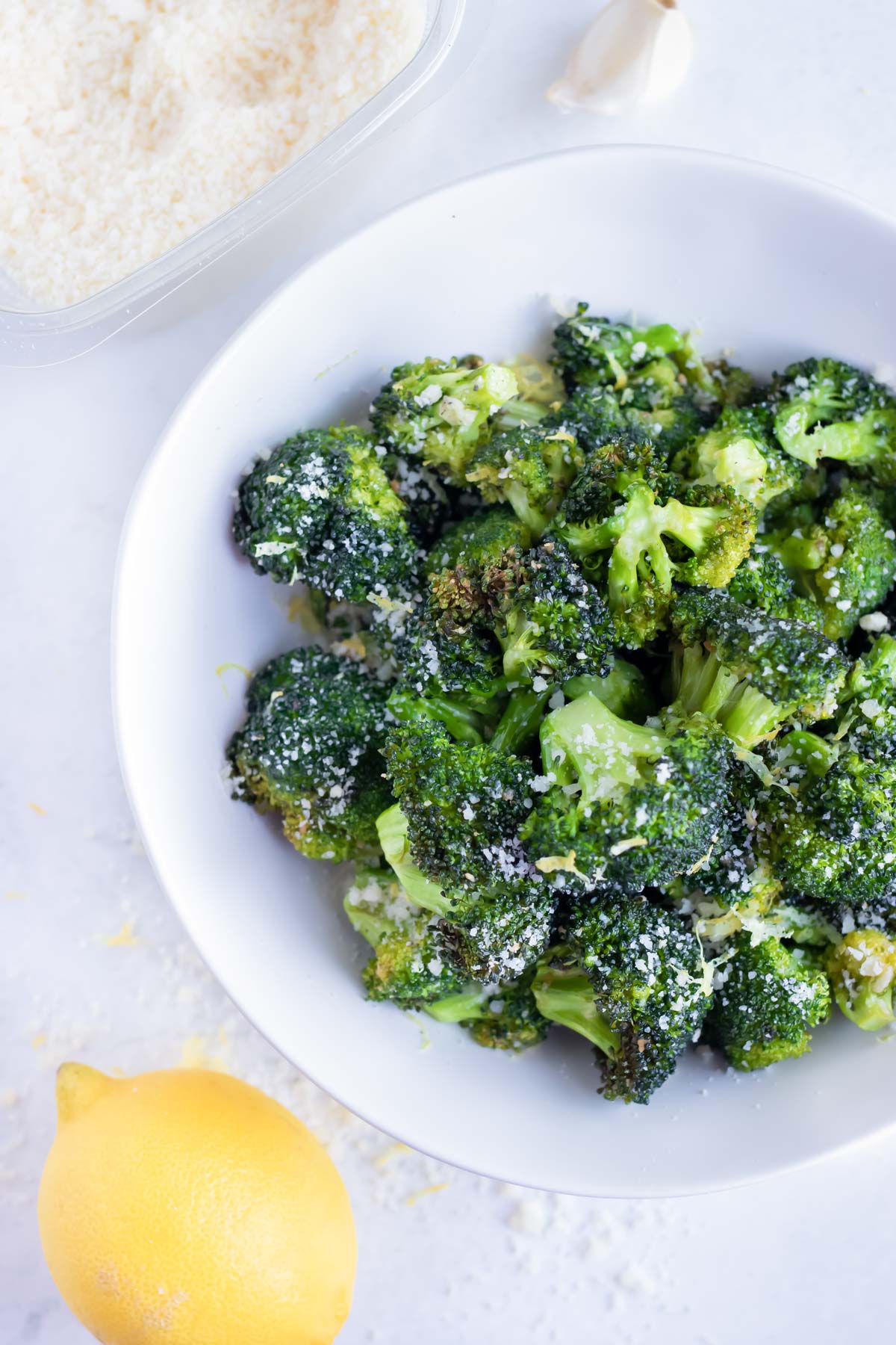 Air fryer broccoli is served on a white plate with grated Parmesan cheese and lemon zest for an easy side dish.