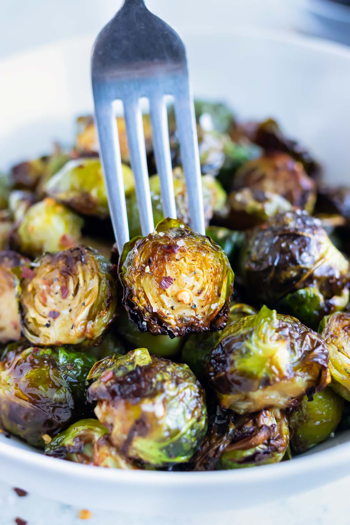 A crispy brussels sprout is lifted up by a fork out of a bowl.